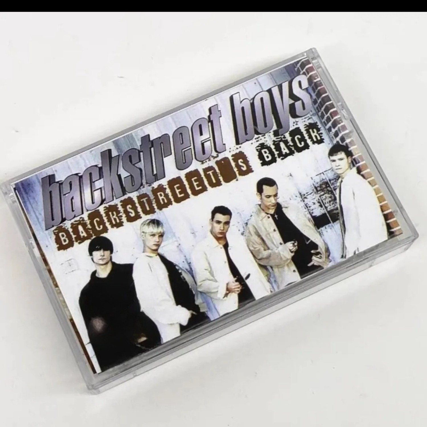 Audio Music Cover - เทปคาสเซ็ตเสียงเพลงป๊อปอะนาล็อกวินเทจ กลุ่มบอยแบนด์ฮาร์โมนี แทร็กเพลงย้อนยุค ปกภาพบุคคลบนกำแพงอิฐ ดนตรีกายภาพที่ชวนให้คิดถึงอดีต